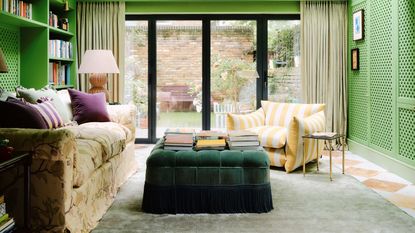 bright light green media room with white and orange terracotta marble checkerboard floor, built-in storage, floral couch, yellow striped armchair and a green velvet fringed trim ottoman