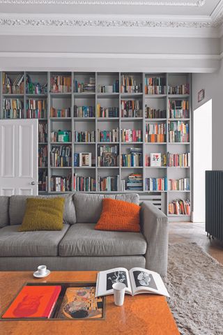 A living room with a grey sofa and a large book case in the background