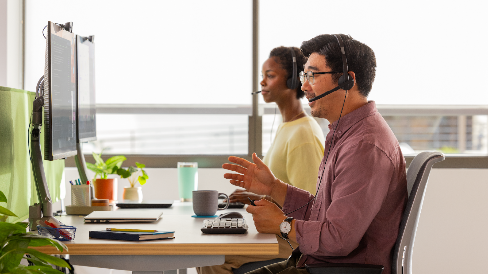 The new Logitech H570e Headset being used by a smiling man and woman. 