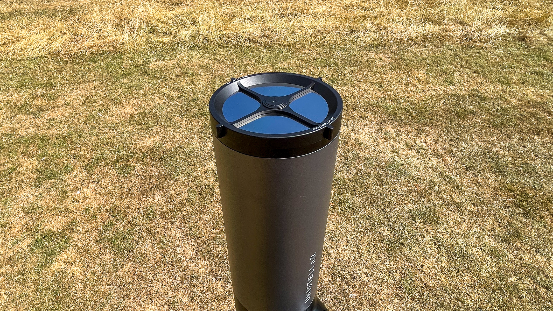 The Unistellar eVscope 2 with solar filter, pointing straight up with grass in the background.