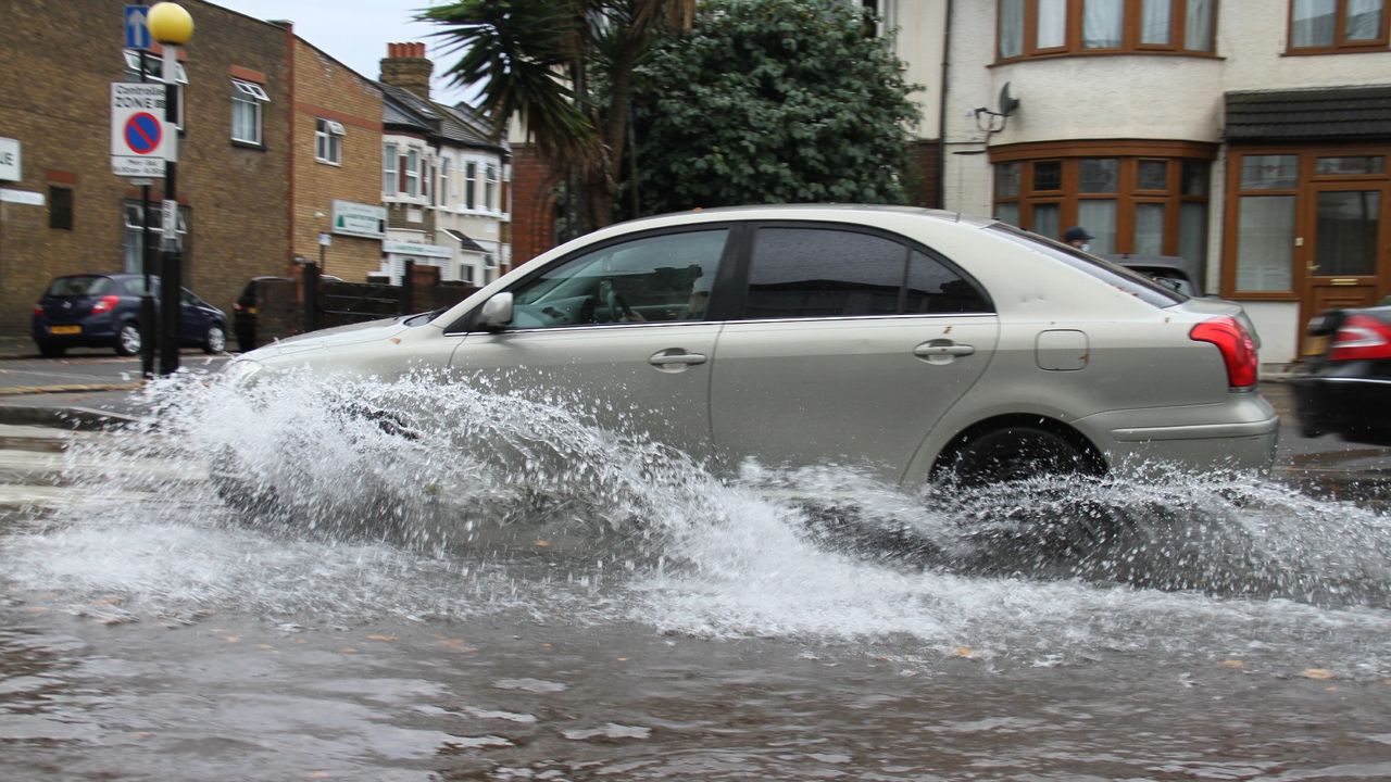 Flooding on a road in East London as a car drives through it following heavy rainfall