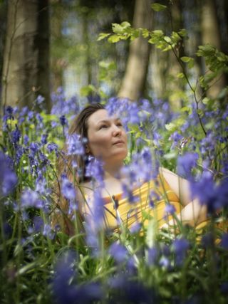 Woman in a yellow dress, lying in a bluebell field with bokeh balls in the background. Shot on the OM System OM-1 Mark II with Pentax Super Takumar 50mm f/1.4 lens