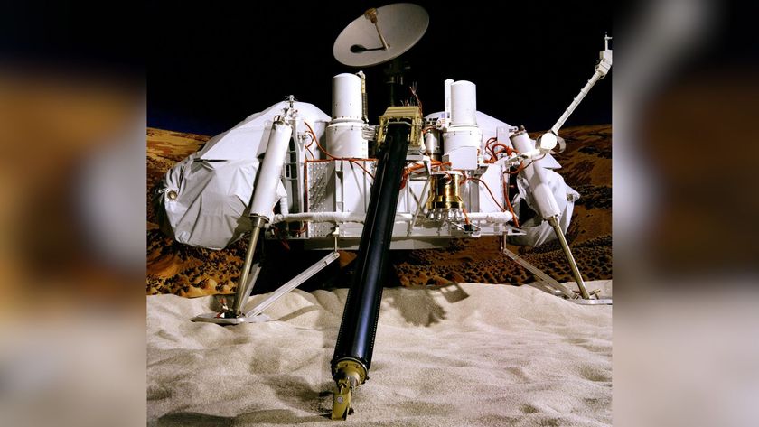 A four-legged orbiter sits on the sand, with a dish and a cloth over its parts.