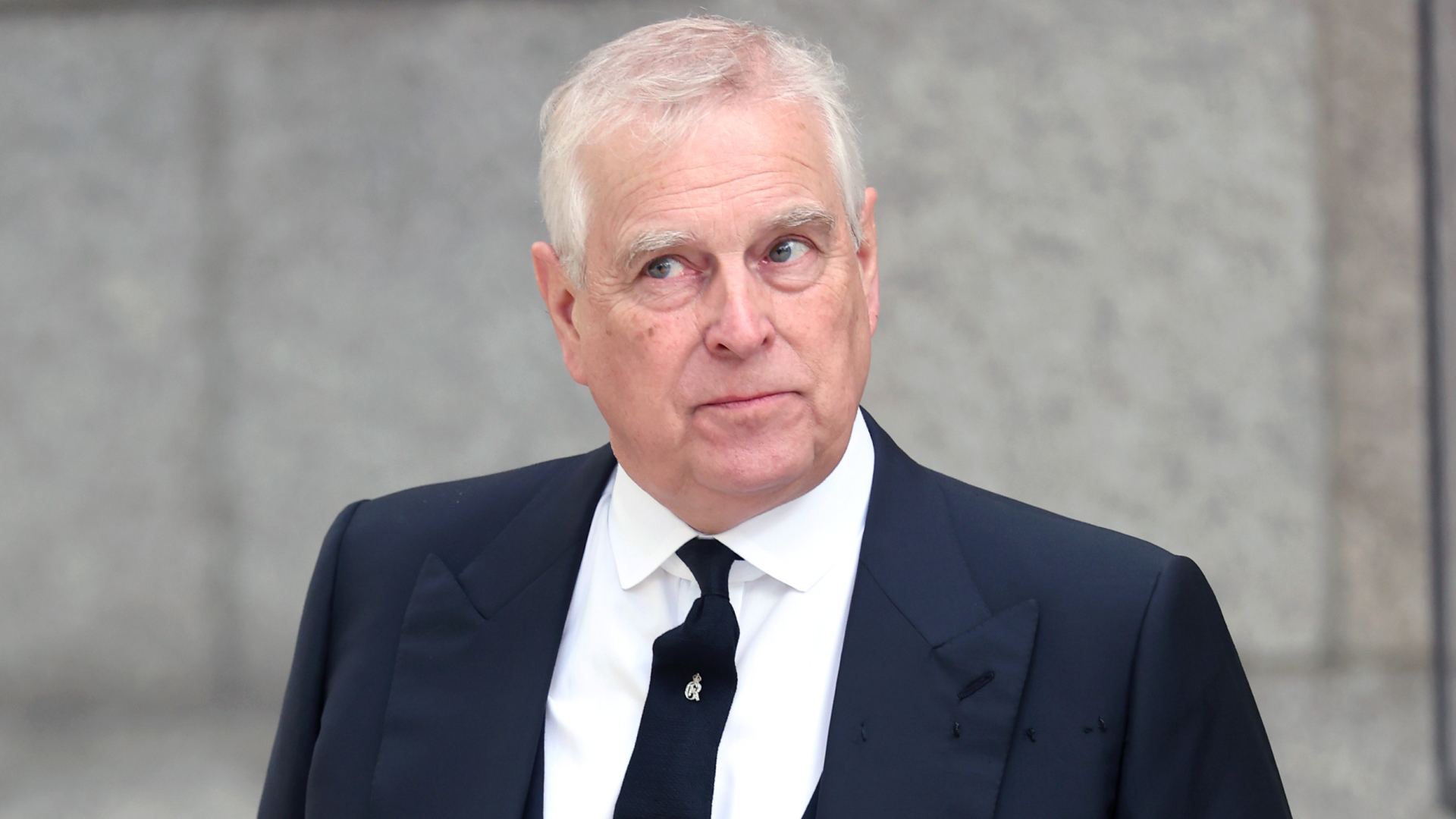 Prince Andrew wears a black suit and matching tie with a white shirt and looks to the sky in a bemused quizzical way