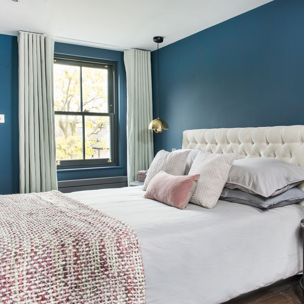 Blue bedroom with cream button backed headboard and grey curtains