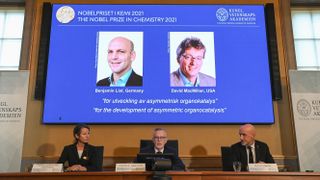 Representatives from the Royal Swedish Academy of Sciences sit in front of a screen displaying the winners of the 2021 Nobel Prize in Chemistry..