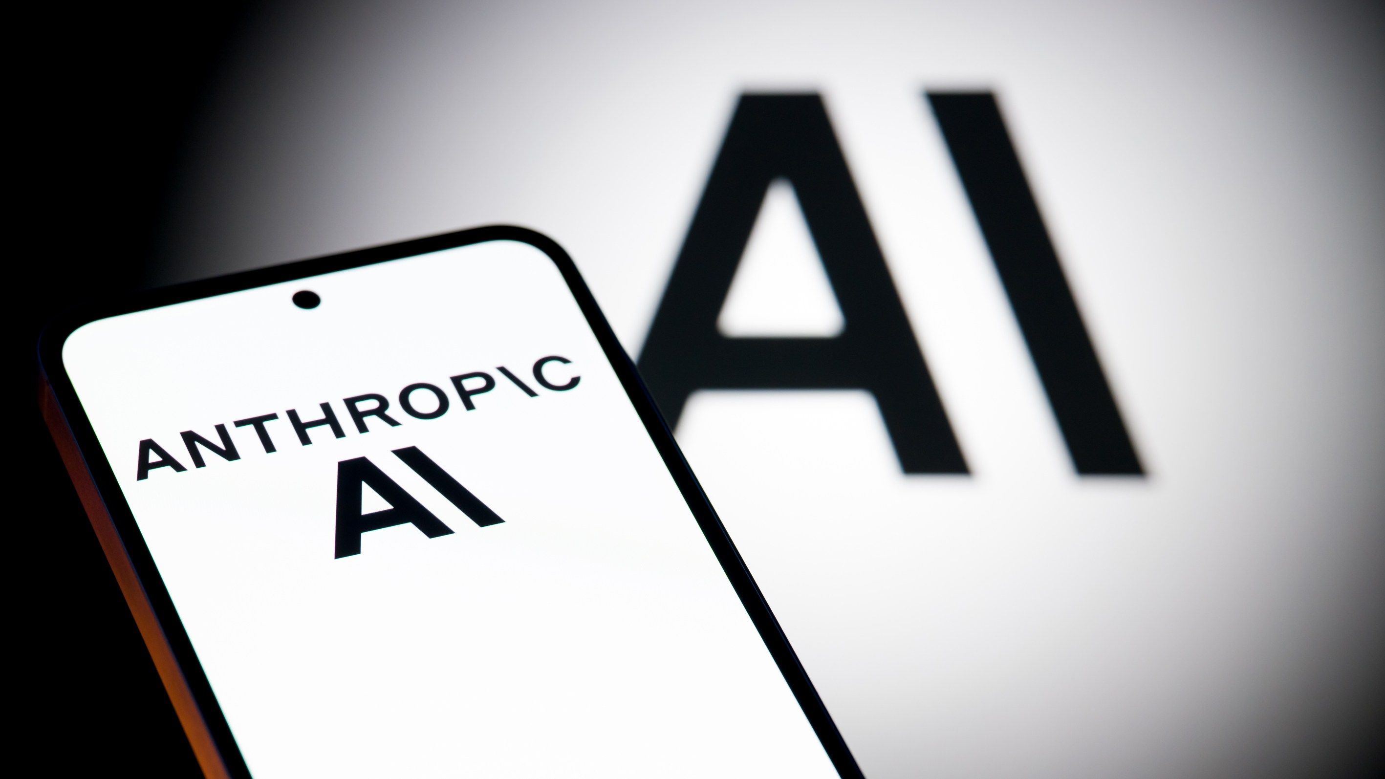The Anthropic AI logo is displayed on a mobile phone with the company AI branding visible in the background, in this photo illustration in Brussels, Belgium, on December 7, 2025. (Photo by Jonathan Raa/NurPhoto via Getty Images)