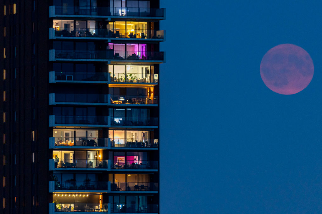 Ein verschwommener roter Mond scheint schwach rechts von einem Hochhaus.