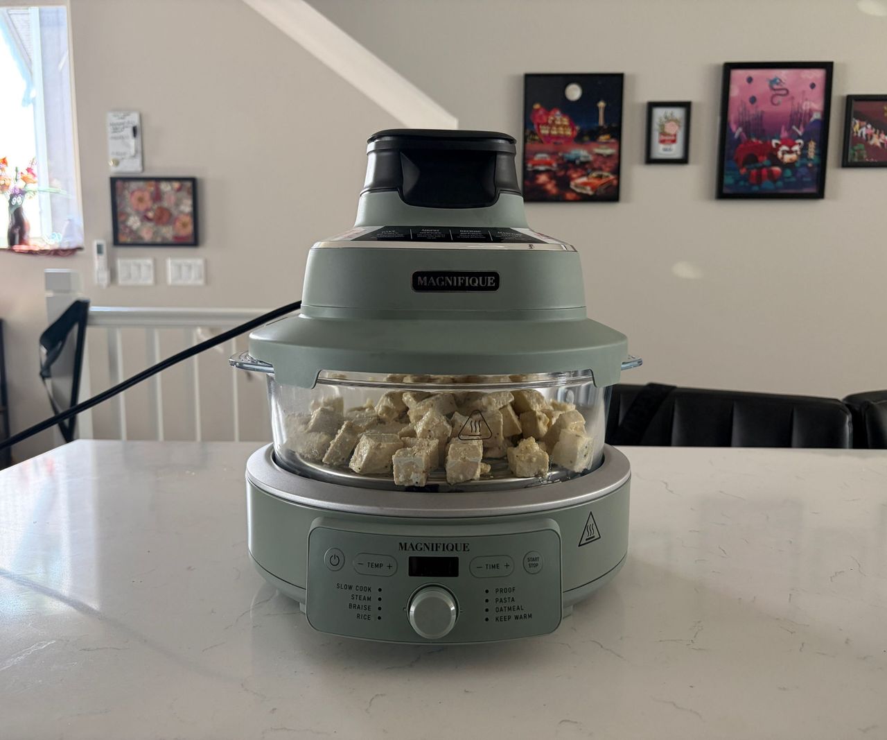 A glass air fryer with a green base on a white countertop filled with tofu.