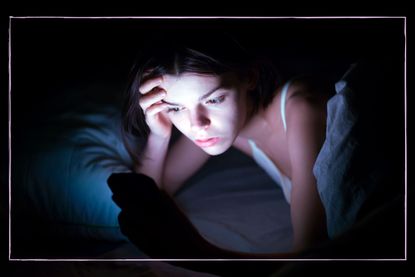 A teenage girl in a dark room lit up by her phone screen