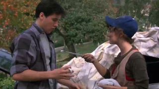 John Cusack being handed a paint brush by a woman in a hat in Better Off Dead.