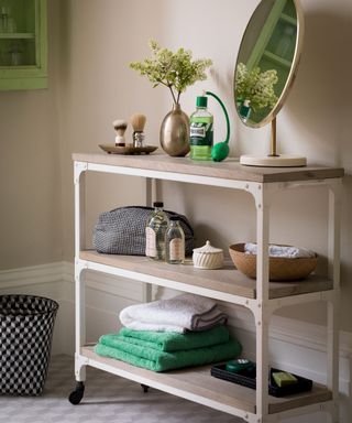 A freestanding bathroom storage trolley with towels and a mirror