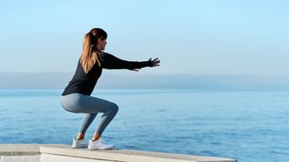 Young woman doing squats with the sea in the background on a sunny day