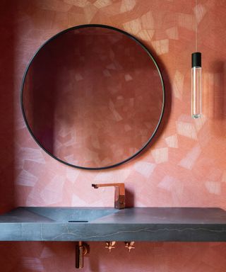 Pink tiled wall in bathroom with gray slate-look waterfall sink and round metal edged mirror on the wall