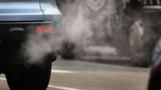 photo shows fumes exiting the tailpipe of a light blue car that appears to be in traffic