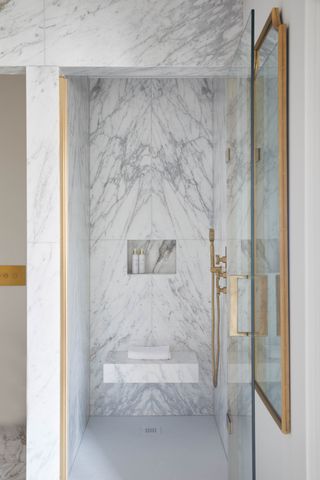 small marble shower with shower bench, brass fixtures and fittings