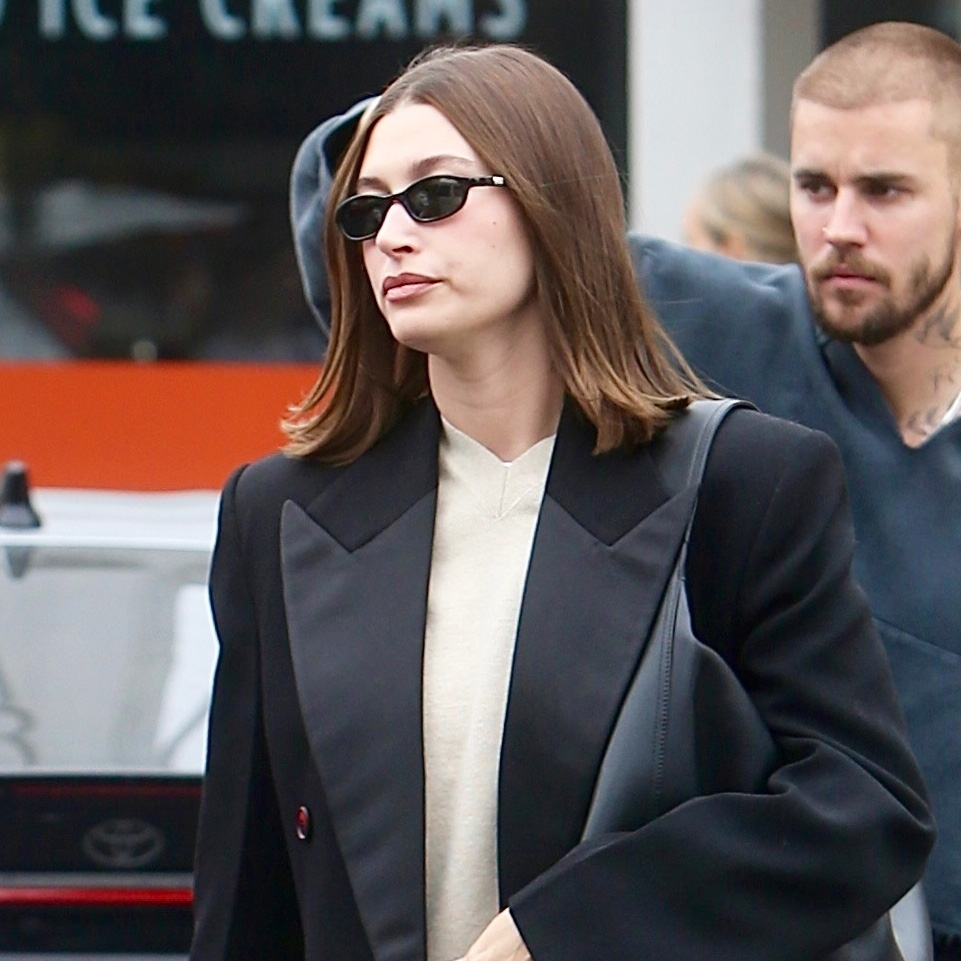 Hailey Bieber wearing a black coat with sweatpants and Ugg Elea slides