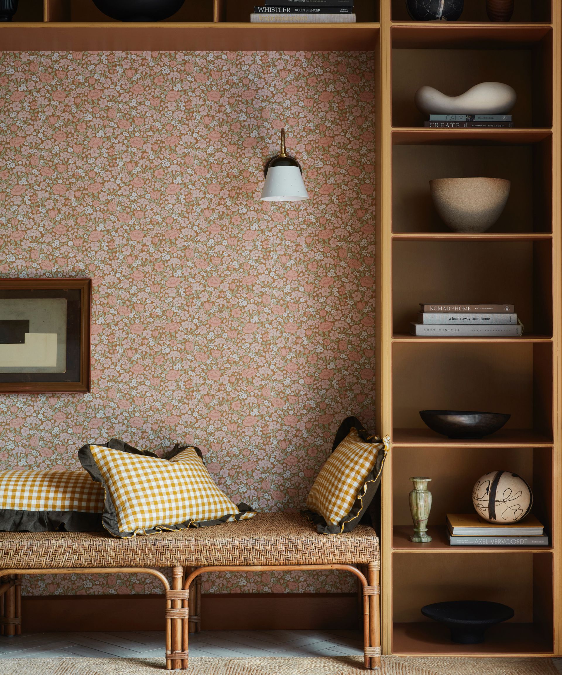living space with ditsy wallpaper and bookcase surrounding bench seating area, tan paint, pendant light, books, ornaments, rattan bench