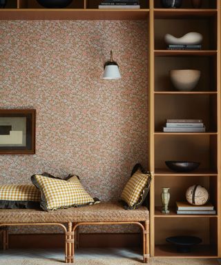 living space with ditsy wallpaper and bookcase surrounding bench seating area, tan paint, pendant light, books, ornaments, rattan bench