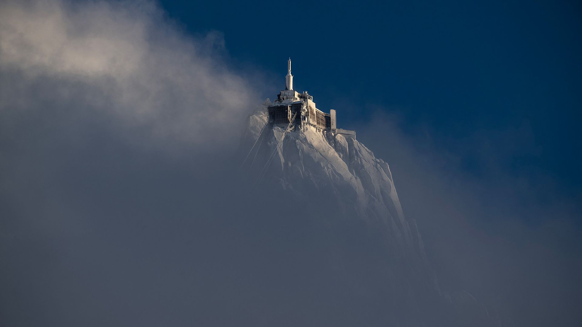 
                                The peak of the Aiguille du Midi mountain rises above clouds in the French Alps, France
                            
