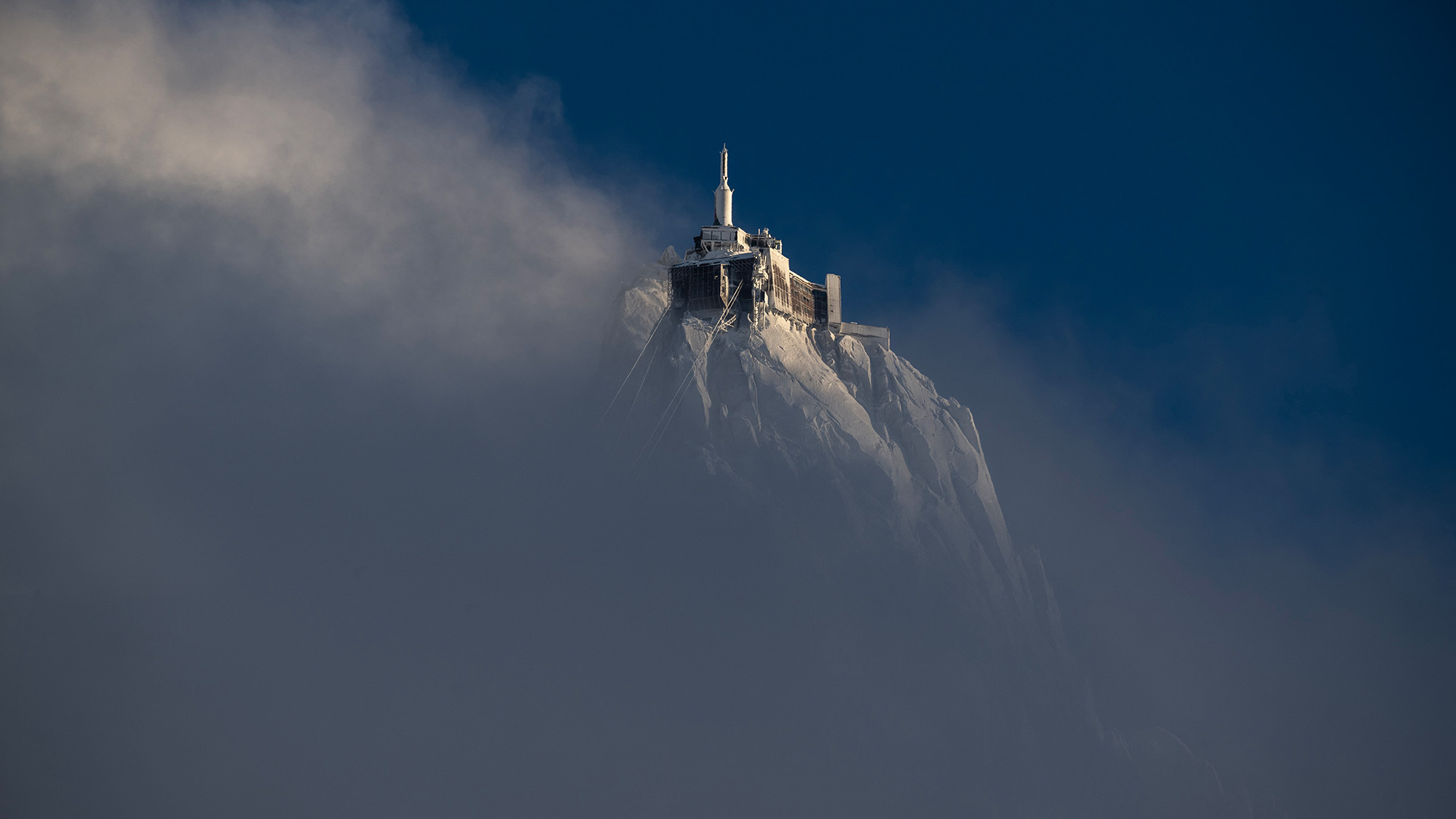 The peak of the Aiguille du Midi mountain rises above clouds in the French Alps, France