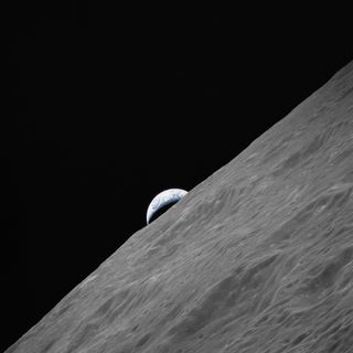 Earth appears in the background just rising above the lunar surface.