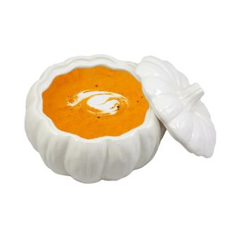 A white ceramic pumpkin shaped bowl with orange pumpkin soup inside of it