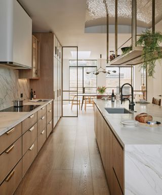 A wooden open plan kitchen with glass panels to zone the kitchen and dining area