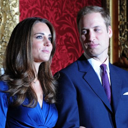 Kate Middleton wears a blue dress and has long curly hair as Prince William looks at her announcing their engagement