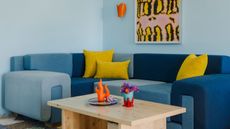 Tonal blue denim sofa against light blue wall with orange sconces and yellow artwork