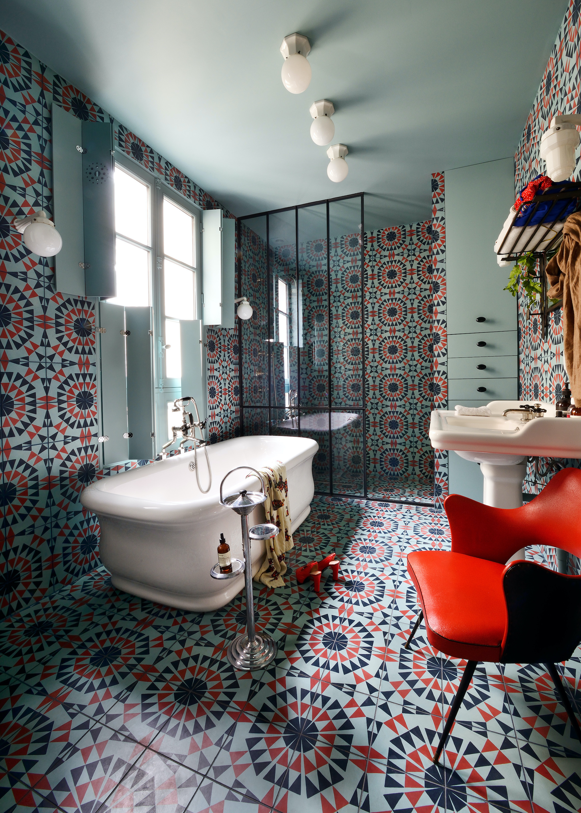 bathroom with vibrant patterned tiles. There is also a bath tub in the corner of the space with a red chair in the side of the room