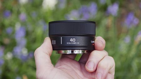 The Panasonic Lumix S 40mm F2 lens in the hand, with natural bluebell backdrop