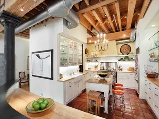 A kitchen with terracotta tiles, wooden beamed ceiling and white cabinetry