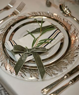 dinner table place setting with silverware, stacked plates with napkin and decorative green velvet bow