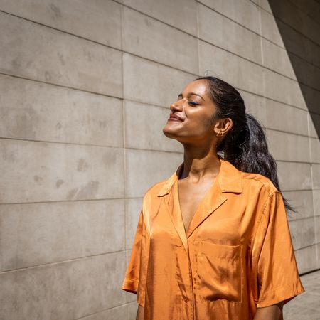 Best glowy sunscreens woman wearing orange shirt looking into the sun looking glowy