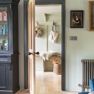 A living room with a black bookcase and antique paintings hanging on the wall with an open door leading into the hallway