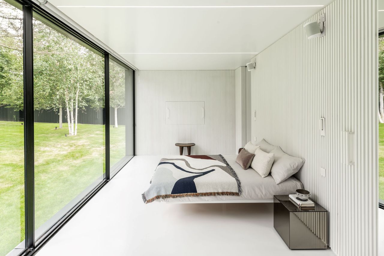Inside the bedroom is a white room with panelled walls and floor to ceiling windows
