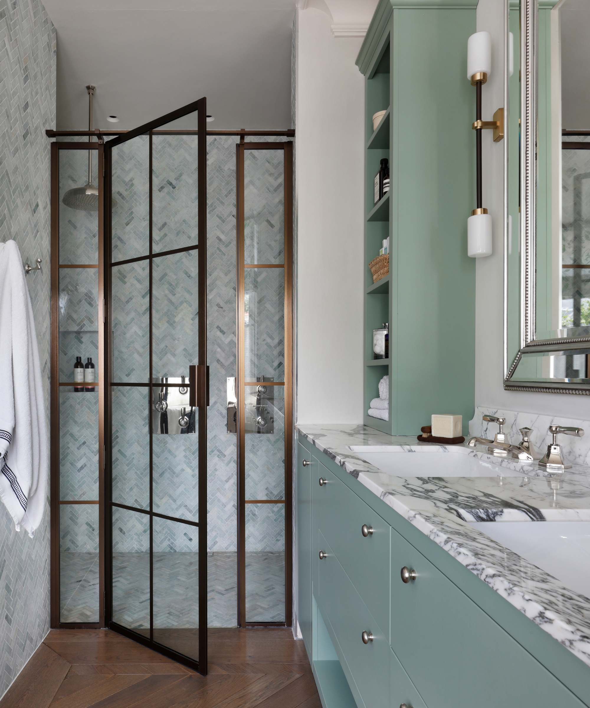 A narrow shower room with a brass and glass shower enclosure and a pale blue vanity and wall shelving unit