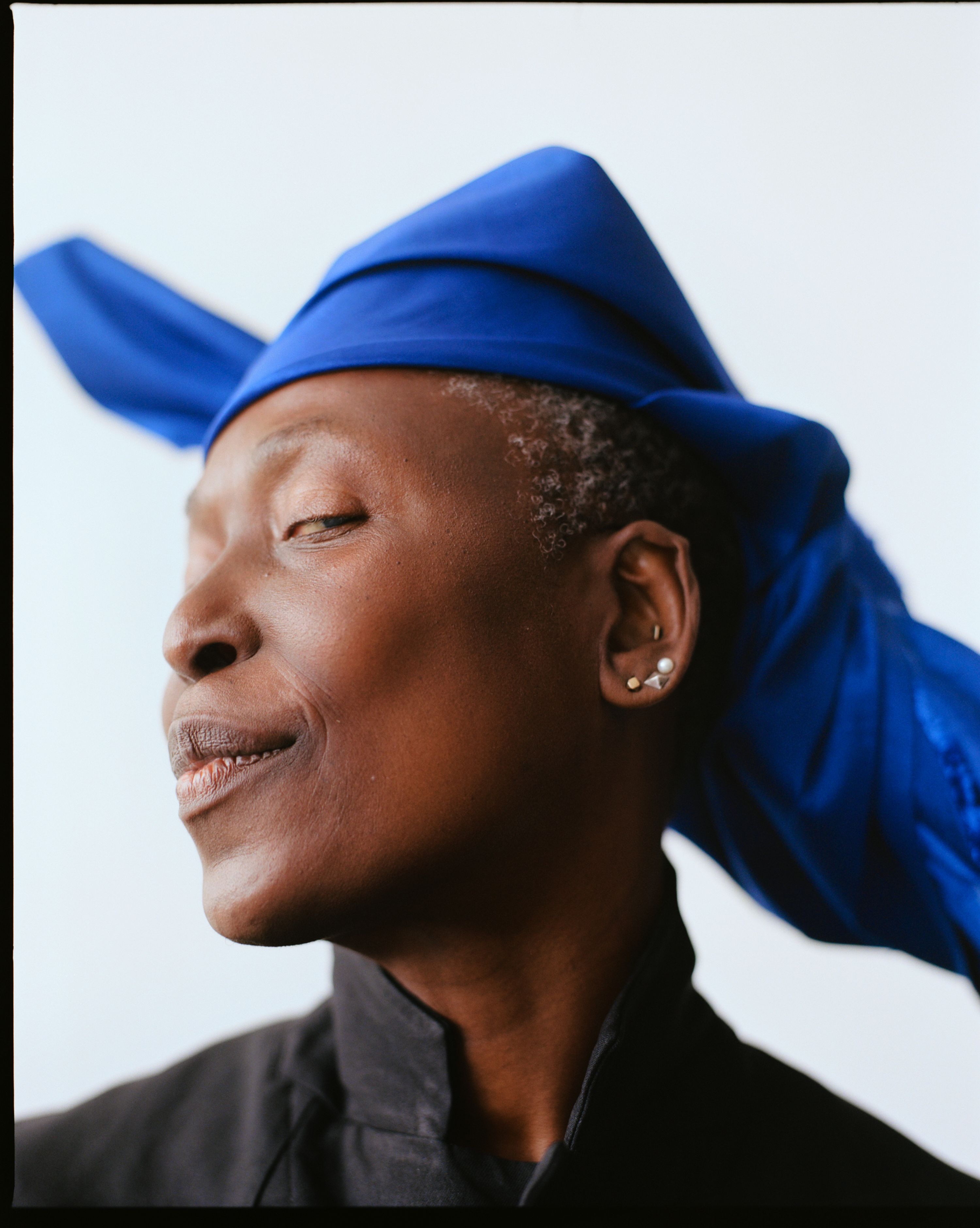 Portrait of nora chipaumire facing to the left, wearing a blue head wrap and black shirt.
