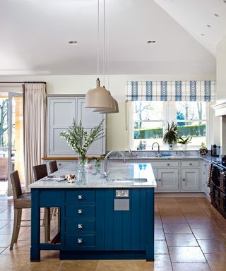A traditional kitchen with an Aga and a navy blue kitchen island and windows and skylights.