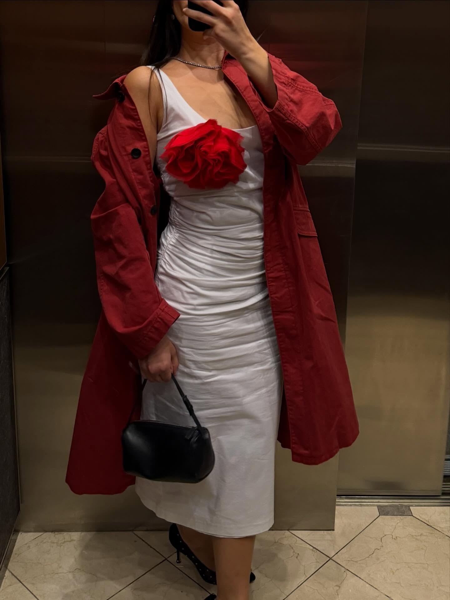 @themillennialdecorator wearing a red trench coat, white dress, and a red flower brooch.
