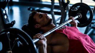 Fit guy performing the bench press exercise in a gym using a barbell
