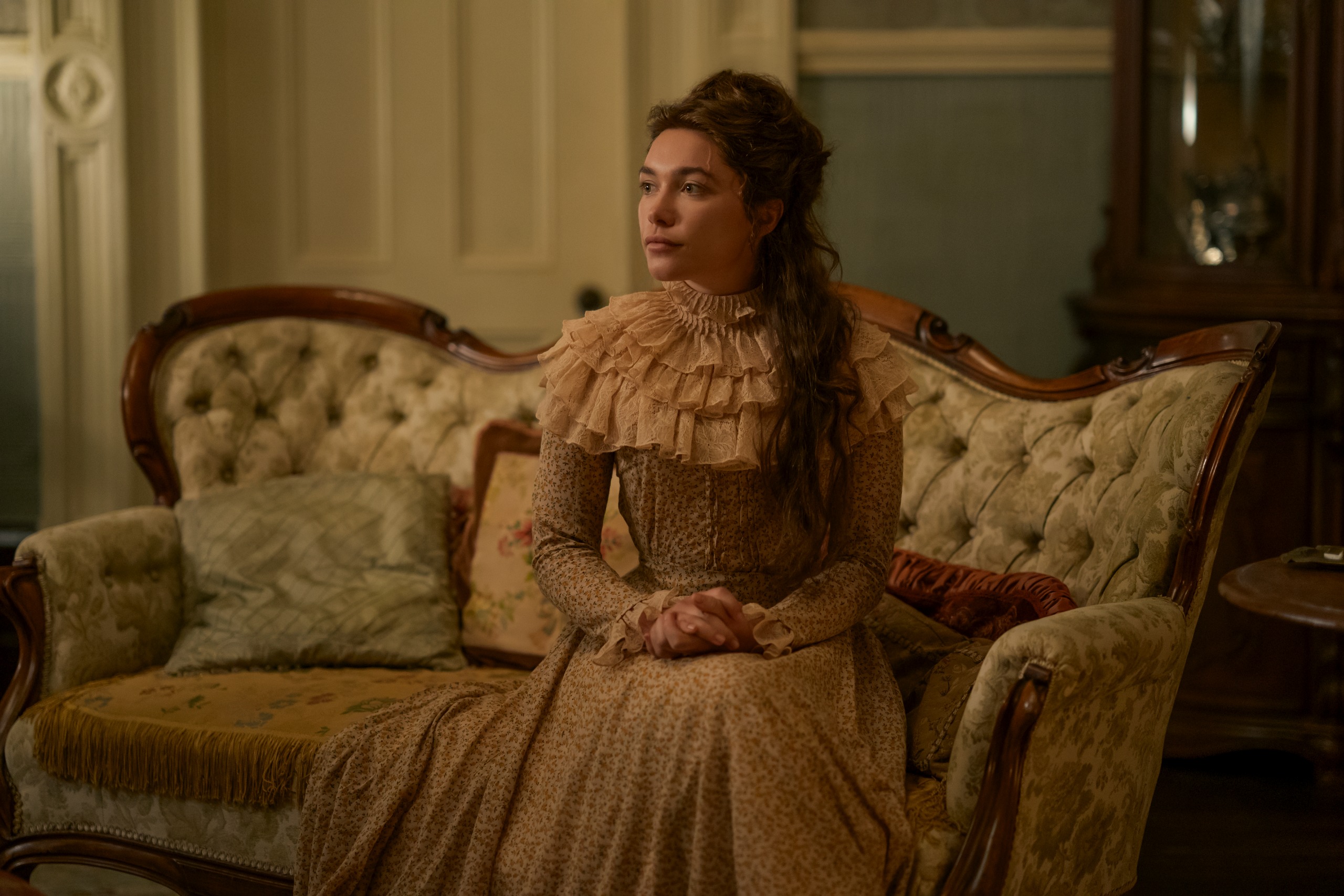 florence pugh as cathy ames wearing a pink long dress sitting on a couch in a parlor in netflix#039;s east of eden