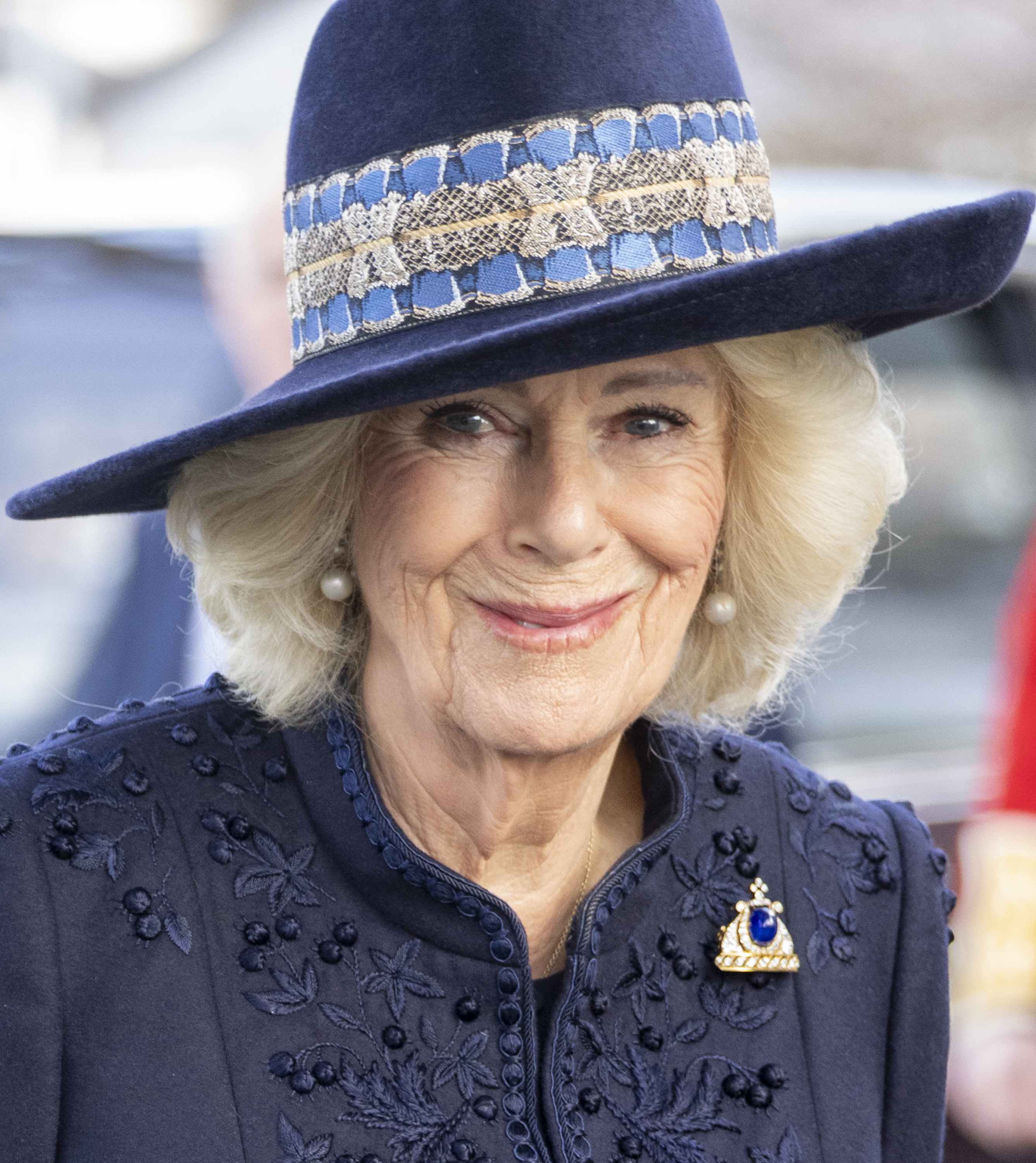Queen Camilla wearing a blue coat and hat and smiling