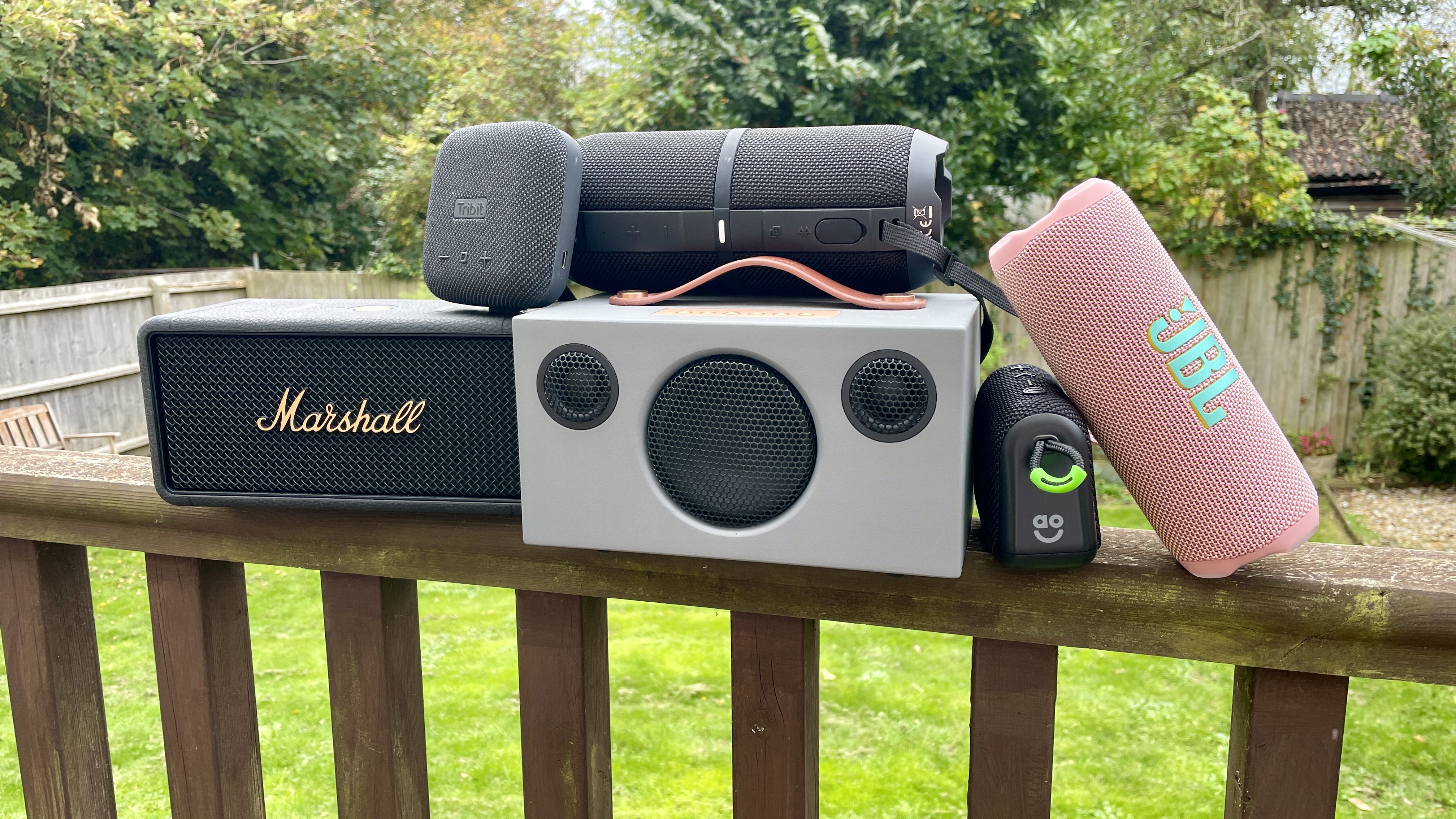 A selection of Bluetooth speakers on a fence, with a garden in the background