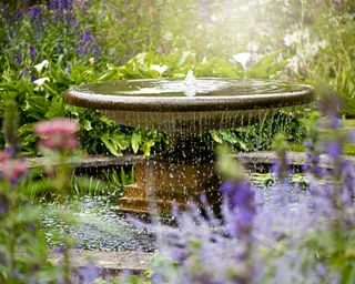 Beautiful summer garden with water fountain in amongst the flowers, in the hazy sunshine