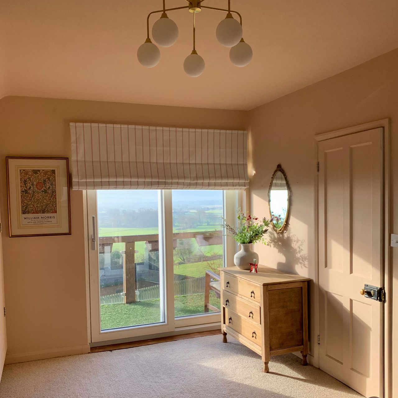 Peach coloured bedroom with striped blind, five light pendant and wooden chest of drawers