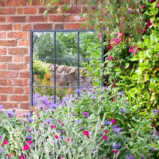 brick wall with window style garden mirror with plants in front