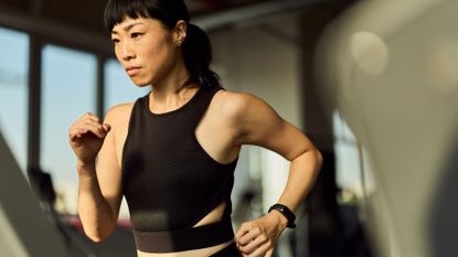 Woman doing Norwegian 4x4 workout on treadmill in gym wearing fitness tracker and sports bra, looking determined