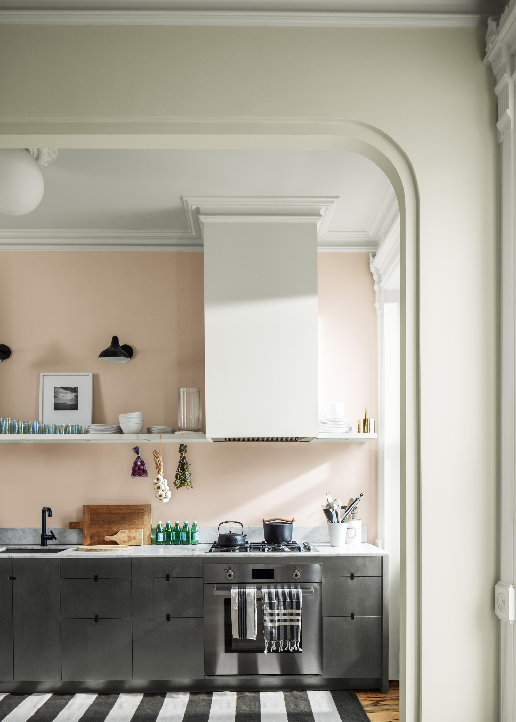 A kitchen with tall ceiling with walls painted in pale pink and kitchen and bottom units in a mid gray, almost steel finish with open shelving above